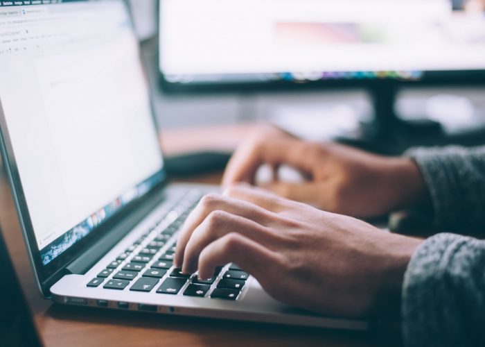 a male transcriptionist's hands are typing on his laptop